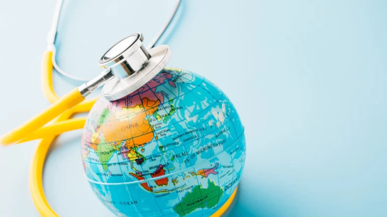 Small toy globe with a yellow and silver stethoscope listening to the globe's heartbeat