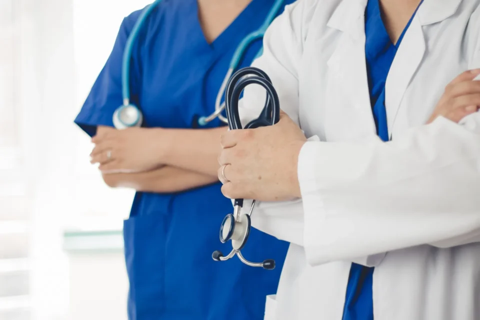 two doctor one wearing white scrubs other wearing blue holding a stethoscope